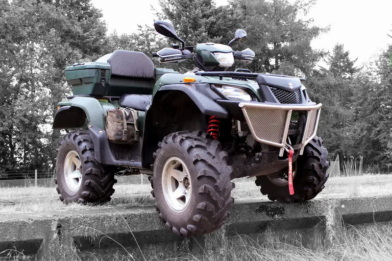 Suzuki KingQuad 750 ATV with an aftermarket front bumper and cargo bags, standing on a concrete block