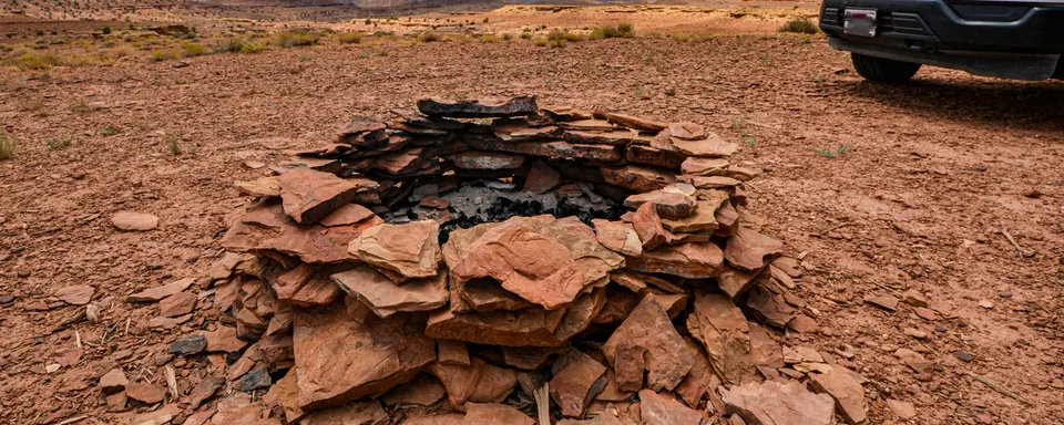A stone fire ring at a dispersed campsite on red desert ground with a pickup parked behind it, San Rafael Swell, Utah
