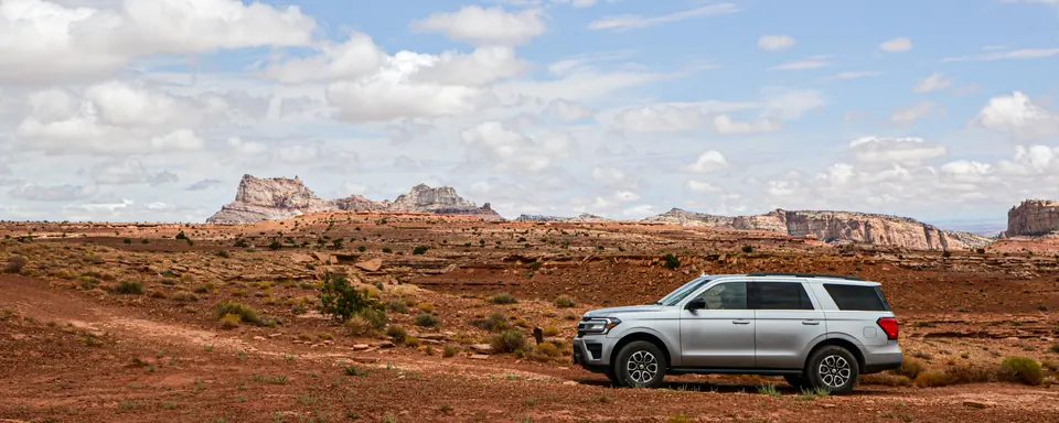 An SUV driving a dirt road toward a dispersed camping area across open desert in the San Rafael Swell, Utah